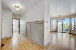 Hallway featuring a notable chandelier, a textured ceiling, and light hardwood / wood-style floors