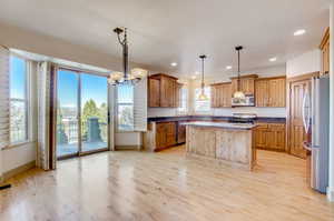 Kitchen with a notable chandelier, a kitchen island, light hardwood / wood-style flooring, and stainless steel appliances