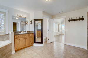 Bathroom with tile flooring, tiled tub, toilet, and vanity