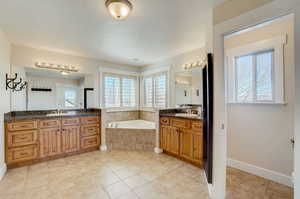 Bathroom featuring a relaxing tiled bath, tile floors, plenty of natural light, and double vanity