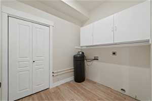 Clothes washing area featuring washer hookup, light hardwood / wood-style floors, electric dryer hookup, and cabinets