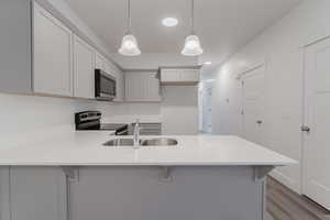 Kitchen featuring sink, light wood-type flooring, a kitchen bar, stainless steel appliances, and pendant lighting