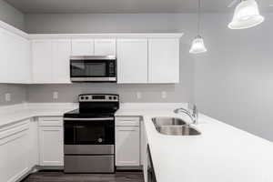 Kitchen with white cabinets, stainless steel appliances, sink, and hanging light fixtures