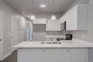 Kitchen with white cabinets, dark hardwood / wood-style flooring, stainless steel appliances, sink, and decorative light fixtures