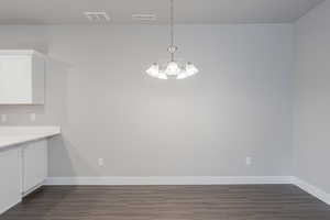 Unfurnished dining area with an inviting chandelier and dark hardwood / wood-style flooring