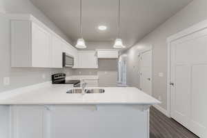 Kitchen with hanging light fixtures, kitchen peninsula, white cabinetry, appliances with stainless steel finishes, and dark hardwood / wood-style flooring