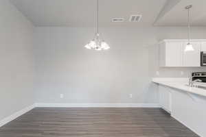 Kitchen with white cabinets, range with electric stovetop, hanging light fixtures, and dark hardwood / wood-style flooring