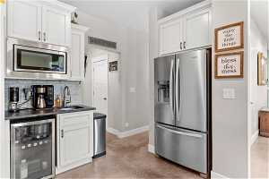 Kitchen featuring tasteful backsplash, white cabinetry, wine cooler, stainless steel appliances, and sink