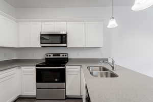 Kitchen featuring white cabinets, sink, decorative light fixtures, stainless steel appliances, and dark stone counters