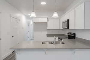 Kitchen featuring hanging light fixtures, sink, white cabinetry, stainless steel appliances, and light stone countertops