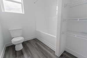 Bathroom with wood-type flooring, tub / shower combination, and toilet