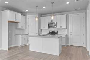 Kitchen featuring pendant lighting, stainless steel appliances, white cabinetry, and light hardwood / wood-style floors