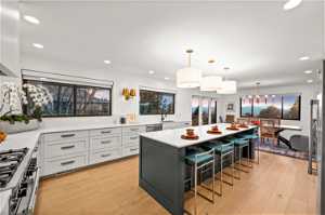 Kitchen with decorative light fixtures, light hardwood / wood-style floors, sink, a center island, and a breakfast bar area