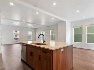 Kitchen with light stone counters, a center island with sink, dishwasher, sink, and dark hardwood / wood-style floors