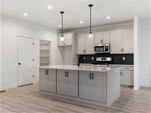 Kitchen with a center island with sink, light hardwood / wood-style floors, appliances with stainless steel finishes, and hanging light fixtures