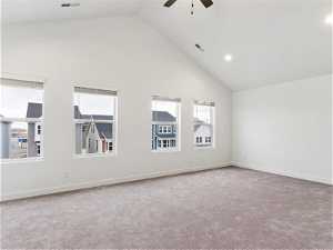 Carpeted empty room with high vaulted ceiling and ceiling fan