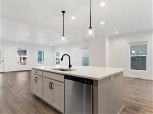 Kitchen with an island with sink, sink, dishwasher, light hardwood / wood-style floors, and decorative light fixtures