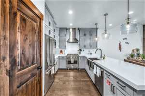 Kitchen with appliances with stainless steel finishes, wall chimney range hood, decorative light fixtures, dark hardwood / wood-style flooring, and sink