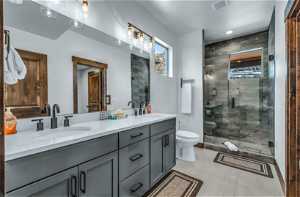 Bathroom with toilet, double sink, vanity with extensive cabinet space, tile floors, and an enclosed shower