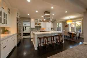 Kitchen with decorative light fixtures, dark wood-type flooring, white cabinetry, island exhaust hood, and backsplash
