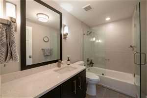 Full bathroom featuring combined bath / shower with glass door, toilet, tile floors, and large vanity