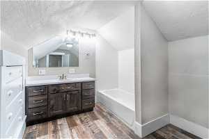 Bathroom featuring hardwood / wood-style floors, a textured ceiling, oversized vanity, and vaulted ceiling