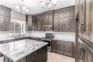 Kitchen featuring a notable chandelier, backsplash, appliances with stainless steel finishes, and a center island