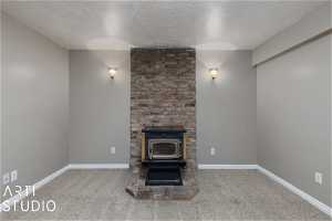 Unfurnished living room featuring a textured ceiling, dark carpet, a wood stove, and brick wall