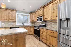Kitchen with sink, stainless steel appliances, tasteful backsplash, decorative light fixtures, and light wood-type flooring