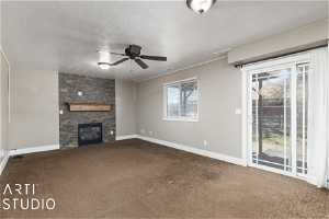 Unfurnished living room with ceiling fan, a stone fireplace, and dark colored carpet