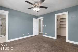 Unfurnished bedroom with dark colored carpet, ensuite bathroom, ceiling fan, a closet, and a walk in closet