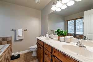 Bathroom with toilet, vanity with extensive cabinet space, dual sinks, tile floors, and tiled tub