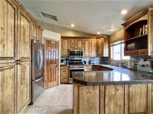 Kitchen with beautifully stained cabinets, peninsula, backsplash, stainless steel appliances, light tile flooring, and vaulted ceiling