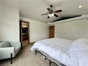 Owners Bedroom with connected en suite, ceiling fan, vaulted ceiling, and light colored carpet