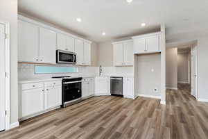 Kitchen featuring backsplash, stainless steel appliances, light hardwood / wood-style floors, and white cabinetry