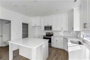 Kitchen with white cabinets, appliances with stainless steel finishes, a kitchen island, and sink