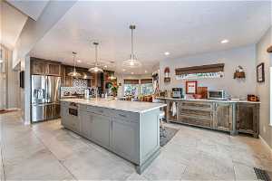 Kitchen featuring backsplash, a kitchen island with sink, stainless steel appliances, light tile floors, and pendant lighting