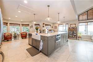 Kitchen featuring custom  leather Quartzite counters, plenty of natural light, light tile floors, hanging light fixtures, and a center island with sink