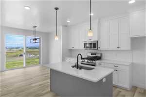 *Kitchen layout is different from home in photo* Kitchen featuring light wood-type flooring, a center island with sink, stainless steel appliances, decorative light fixtures, and white cabinetry