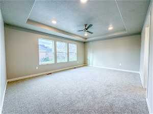 Carpeted spare room with a tray ceiling, ceiling fan, and a textured ceiling