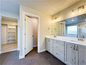Bathroom with double sink, a textured ceiling, tile floors, and vanity with extensive cabinet space