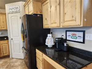 Kitchen featuring natural Knotty Alder cabinets, black fridge, dark granite countertops