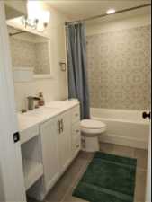 Full bathroom with tile flooring, large vanity, shower / bath combo with shower curtain, and tasteful backsplash