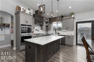 Kitchen featuring hanging light fixtures, dark hardwood / wood-style floors, stainless steel appliances, a center island, and tasteful backsplash