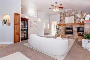 Carpeted living room with ceiling fan, a textured ceiling, vaulted ceiling, and a stone fireplace