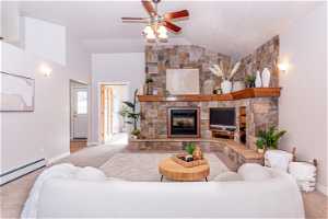 Carpeted living room featuring ceiling fan, a baseboard radiator, a fireplace, and vaulted ceiling