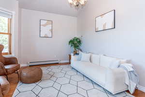 Living room featuring light wood-type flooring, a baseboard heating unit, lofted ceiling, and a chandelier