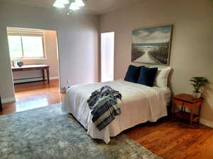 Bedroom with ceiling fan, ornamental molding, hardwood / wood-style flooring, and a baseboard heating unit