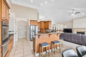 Kitchen featuring ceiling fan, a kitchen breakfast bar, appliances with stainless steel finishes, dark stone countertops, and light tile floors