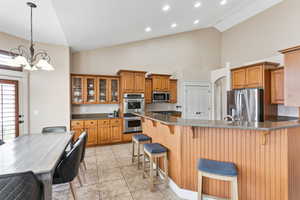 Kitchen featuring an inviting chandelier, a breakfast bar area, light tile floors, stainless steel appliances, and pendant lighting